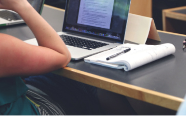 student looking at computer screen with notepad and pen next to it.